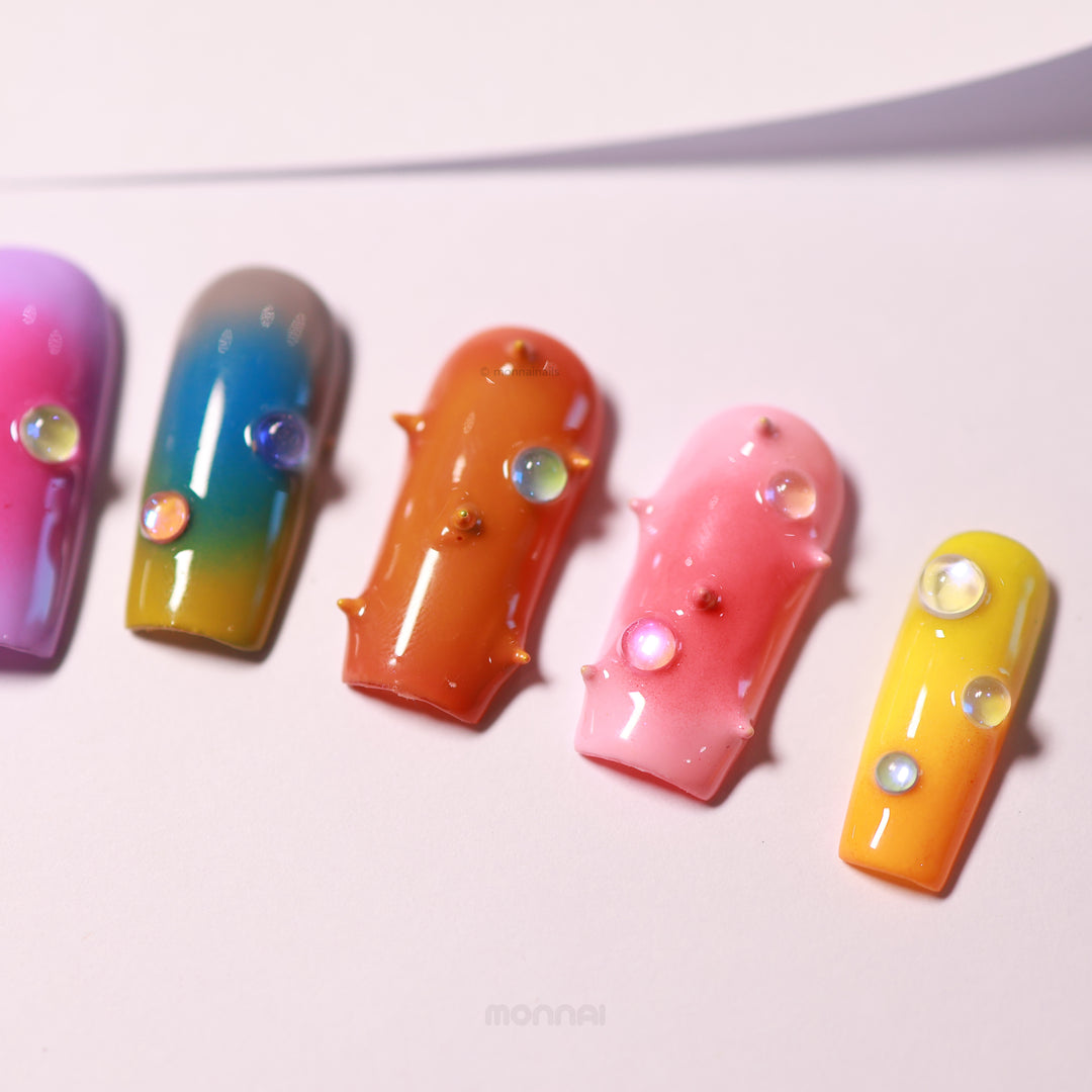 Neon Studs press-on nails laid out in close-up, featuring mismatched aura gradients, 3D studs, and iridescent bead accents.