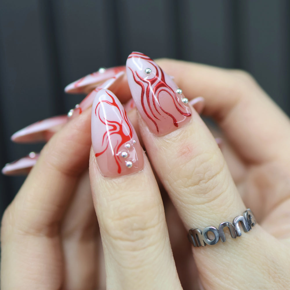 Neural Flux press-on nails on hand with red swirls, silver beads, and a sheer nude base