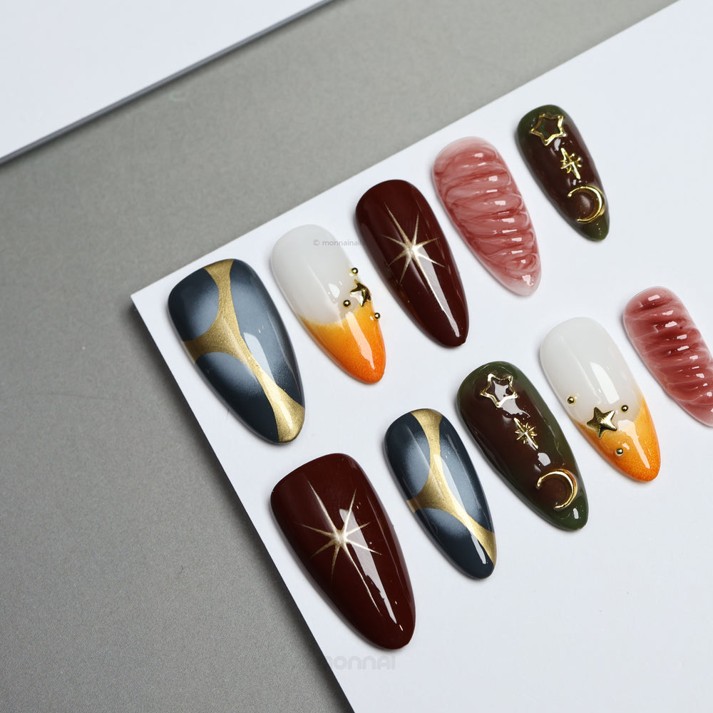 Nocturne press-on nails laid out with moody burgundy, slate blue, olive, nude and gold star and moon details.