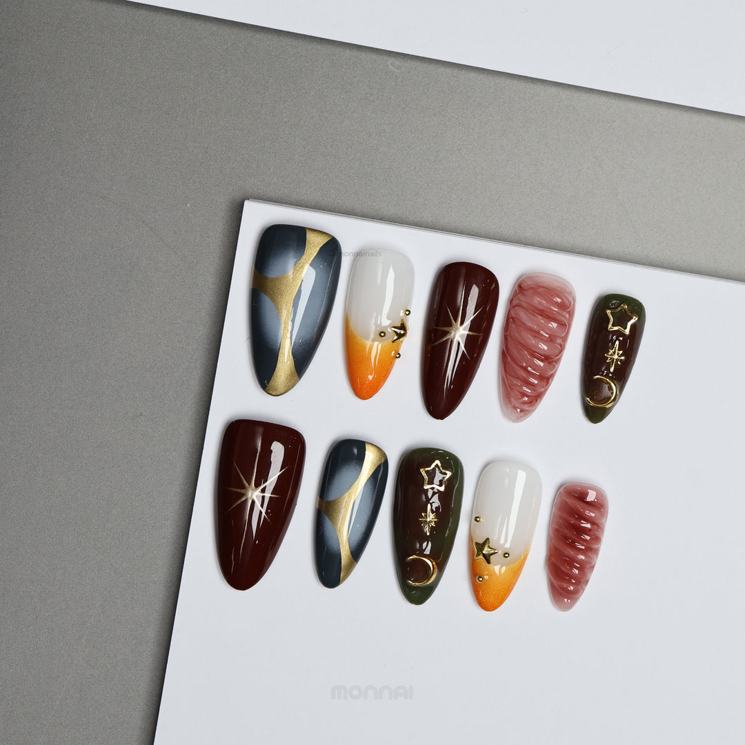 Nocturne press-on nails displayed on a card, featuring moody burgundy, slate blue, olive, nude, and gold star and moon details.