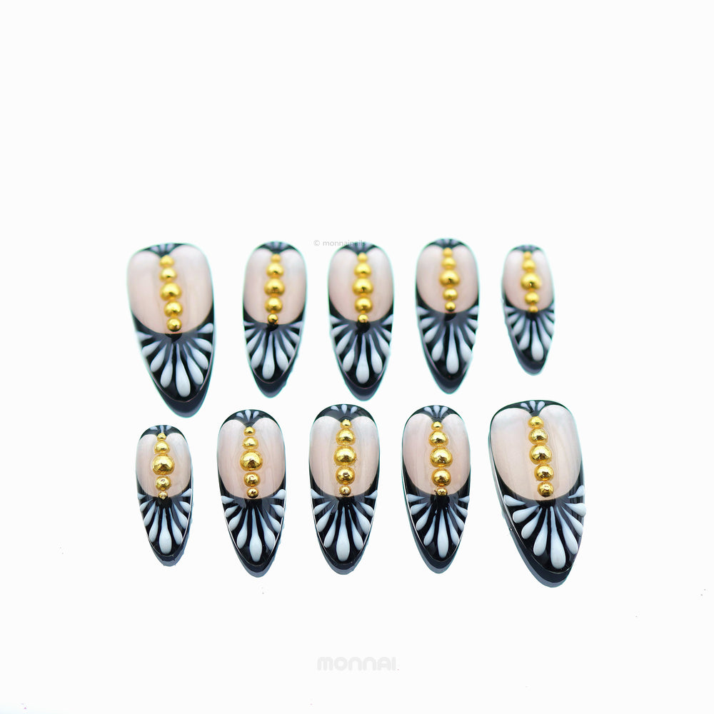 Noir Chic press-on nails laid out, showing nude centers, black-and-white fan patterning, and tiny gold beads.