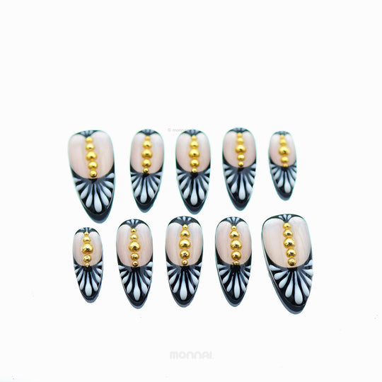 Noir Chic press-on nails laid out, showing nude centers, black-and-white fan patterning, and tiny gold beads.