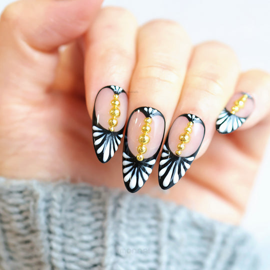 Noir Chic press-on nails worn on hand, with black-and-white fan pattern and gold beads on nude center.