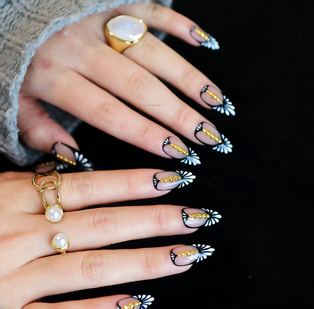 Noir Chic press-on nails on hands, nude base with black fan pattern and gold bead accents