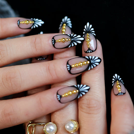 Noir Chic press-on nails worn on hands, with nude centers, black-and-white fan patterning, and gold bead accents.