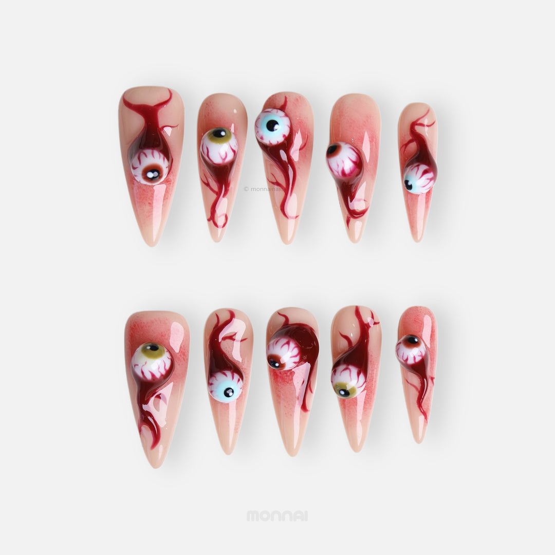 O-O press-on nails in close-up, laid out with surreal 3D eyeball charms, skin-tone base, and blood drip details