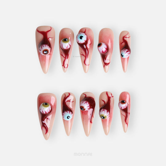 O-O press-on nails in close-up, laid out with surreal 3D eyeball charms, skin-tone base, and blood drip details