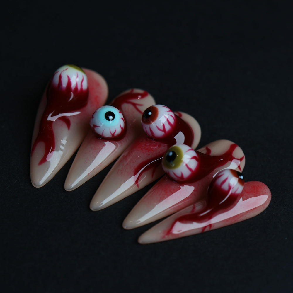 O-O press-on nails with 3D eyeball charms, blood drip details, and skin-tone bases in a surreal hyper-realistic close-up.