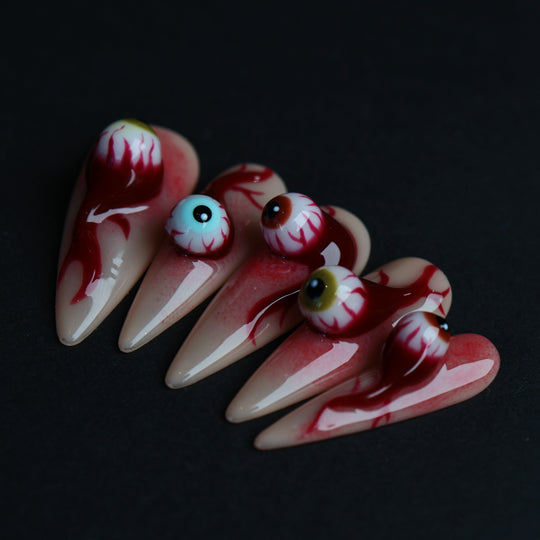 O-O press-on nails with 3D eyeball charms, blood drip details, and skin-tone bases in a surreal hyper-realistic close-up.