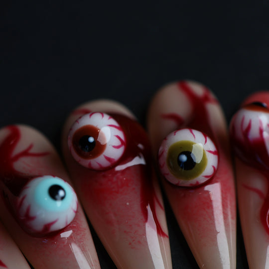 O-O press-on nails close-up with 3D eyeball charms, hand-painted red veins, and glossy grotesque skin-tone nails.