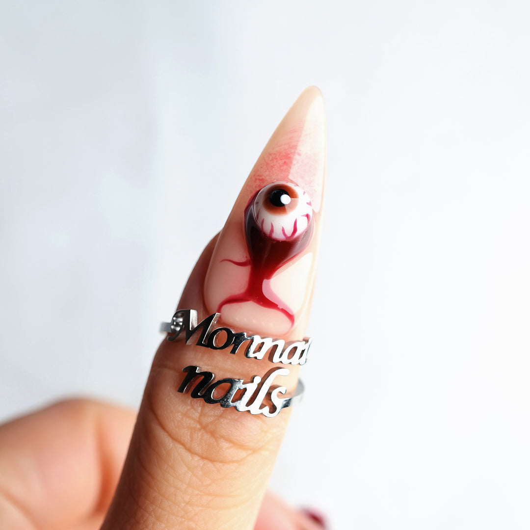 O-O press-on nails, close-up of a surreal eyeball charm nail with skin-tone base and blood drip detail