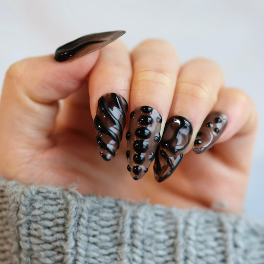 Obsidian Mist press-on nails on hand, sheer nude with black abstract gel lines and glossy bead accents
