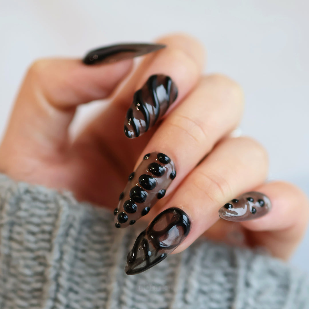 Obsidian Mist press-on nails worn on hand, with sheer nude base, glossy black gel lines and bead accents.