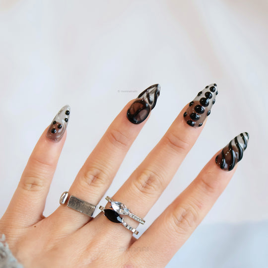 Obsidian Mist press-on nails worn on hand, sheer nude base with abstract black gel lines and glossy bead accents