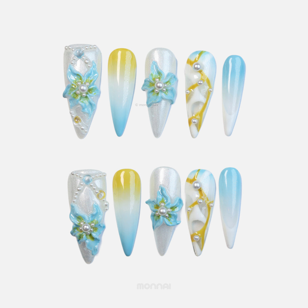 Ocean Breeze press-on nails laid out in sculptural luminescence, silver cat-eye, blue florals, pearls, and yellow-blue gradient