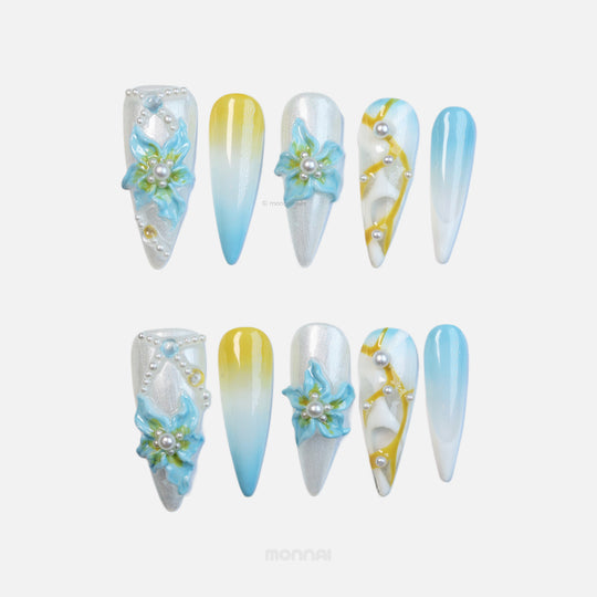 Ocean Breeze press-on nails laid out in sculptural luminescence, silver cat-eye, blue florals, pearls, and yellow-blue gradient