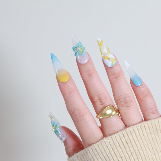 Ocean Breeze press-on nails worn on hand, with soft yellow and pastel blue gradient, blue florals, pearls, and glossy finish.