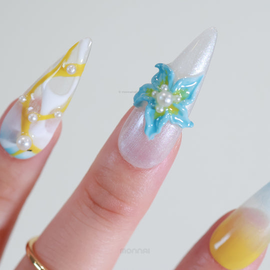 Ocean Breeze press-on nails worn on fingers, with sculptural blue florals, pearls, and a soft yellow-blue gradient.