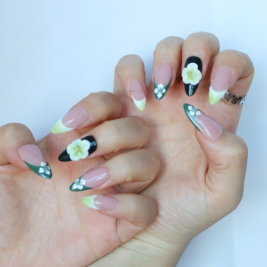 Olive Petal press-on nails worn on hands, with nude bases, green French tips, white flowers, and a black accent nail.