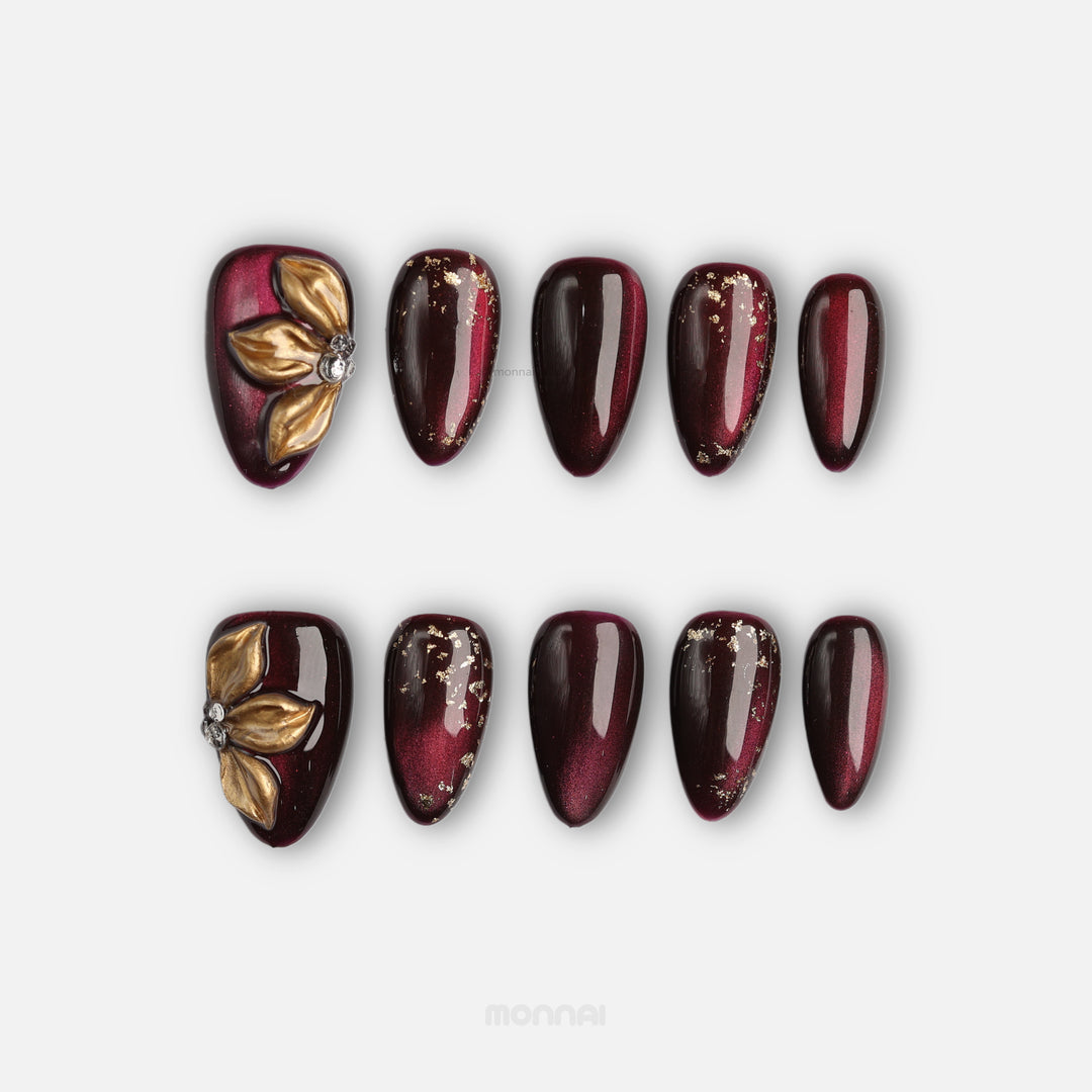 Opulent Noir press-on nails laid out, deep burgundy cat-eye shimmer with gold floral accent and foil details