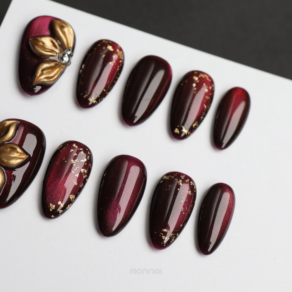 Opulent Noir press-on nails laid out in deep burgundy cat-eye shimmer with gold foil accents
