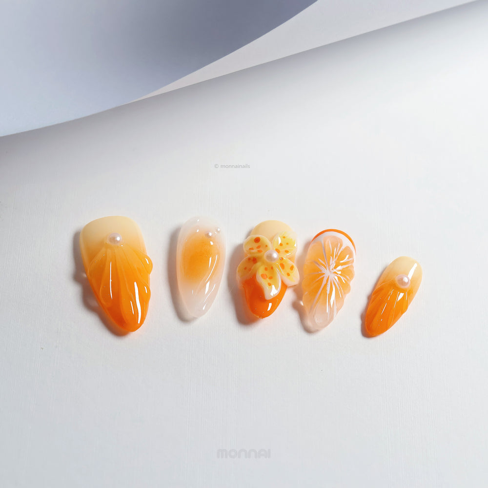 Orange Blossom press-on nails laid out in close-up, with orange citrus art, sheer bases, and 3D flower details.
