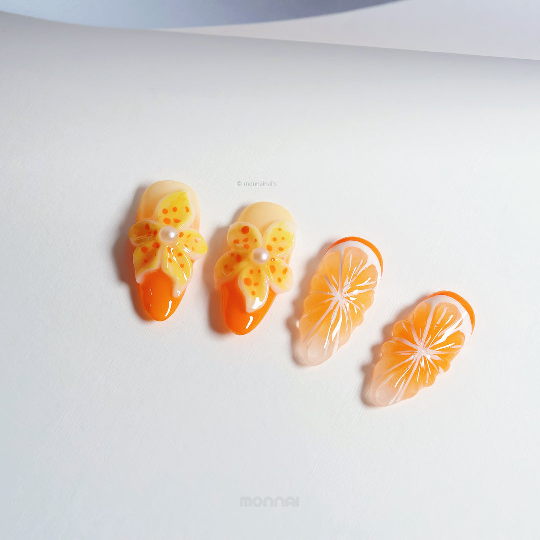 Orange Blossom press-on nails laid out, with glossy orange citrus slices and 3D blooming floral accents.