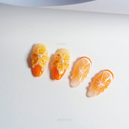 Orange Blossom press-on nails laid out, with glossy orange citrus slices and 3D blooming floral accents.