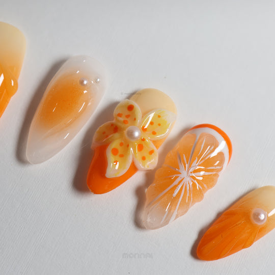 Orange Blossom press-on nails laid out in close-up, with sheer orange citrus art, 3D flower, and orange slice details