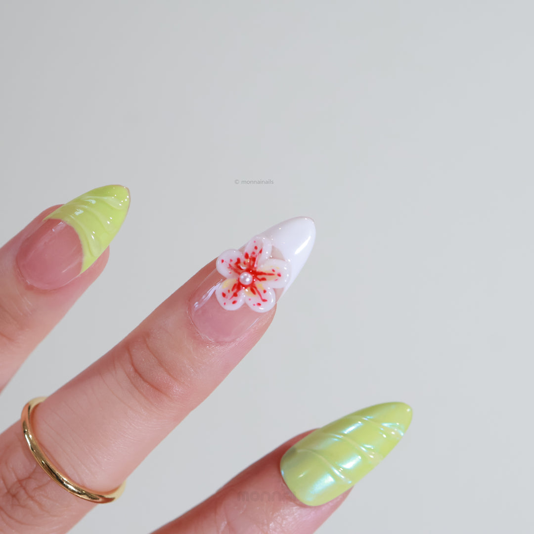 Orchid Glow press-on nails worn on hand, showing neon green tips and a white floral accent with red details.