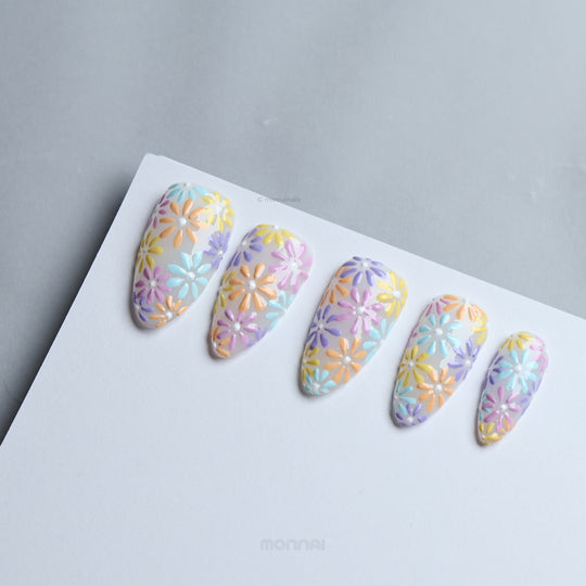 Pastel Meadow press-on nails laid out, showing milky white bases with pastel flower patterns in blue, yellow, pink, orange, and violet.