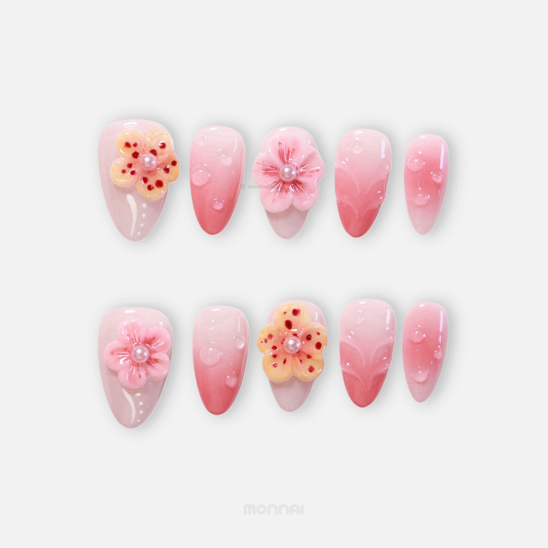 Peach Petals press-on nails laid out, soft pink ombre with 3D flowers, water droplets, and pearls