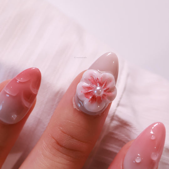 Peach Petals press-on nails in close-up, with soft pink ombre, water droplets, and a 3D flower pearl accent.