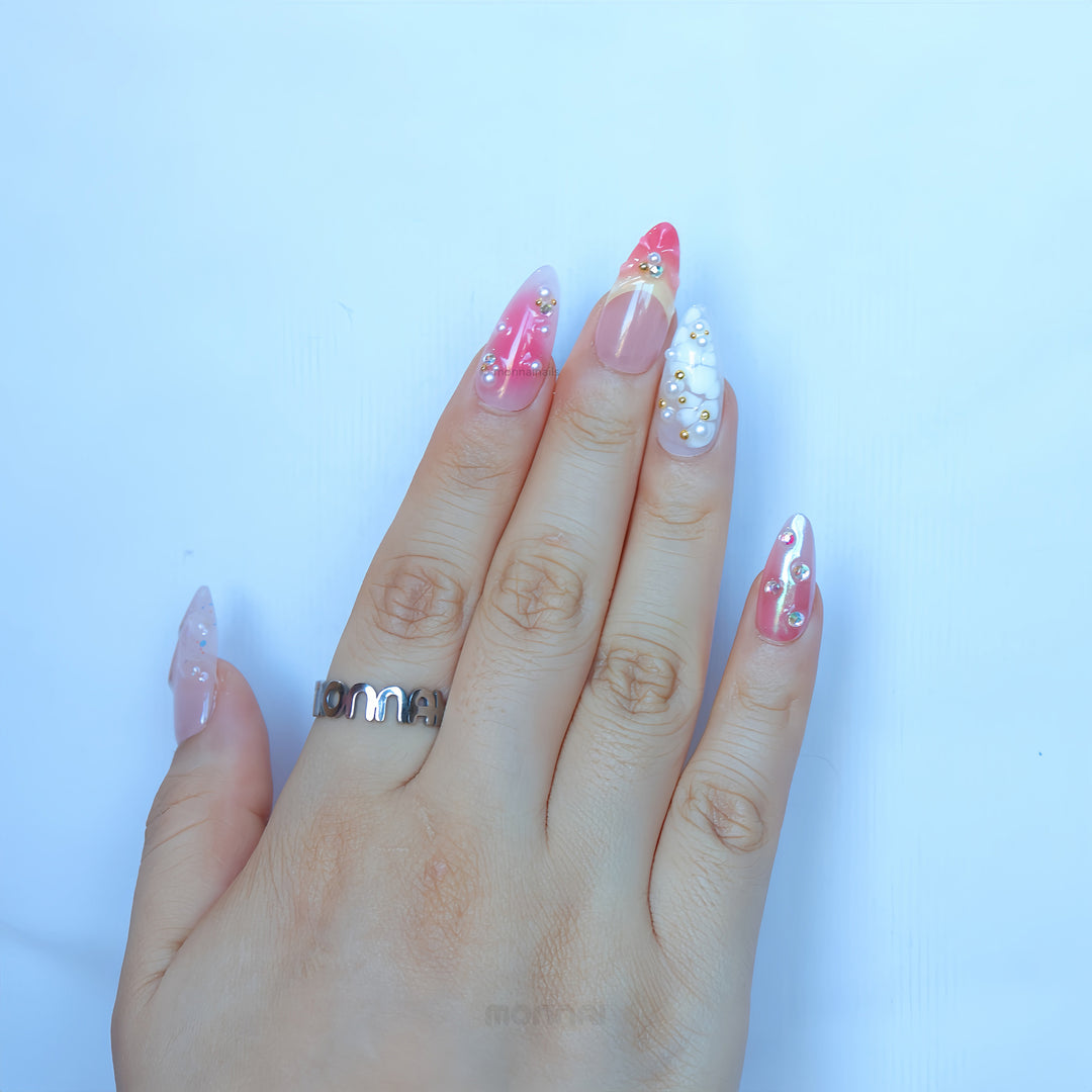 Pearl Diaries press-on nails worn on hand with sheer pink shimmer, milky white French tips, pearls, and crystal accents