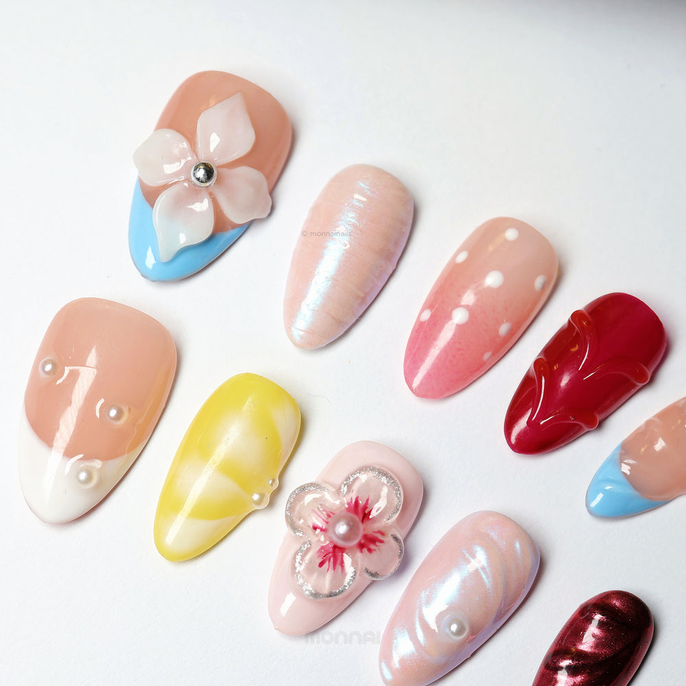 Petal Dream press-on nails laid out in mixed nude, ruby, and pastel designs with 3D flowers, chrome, and pearl accents