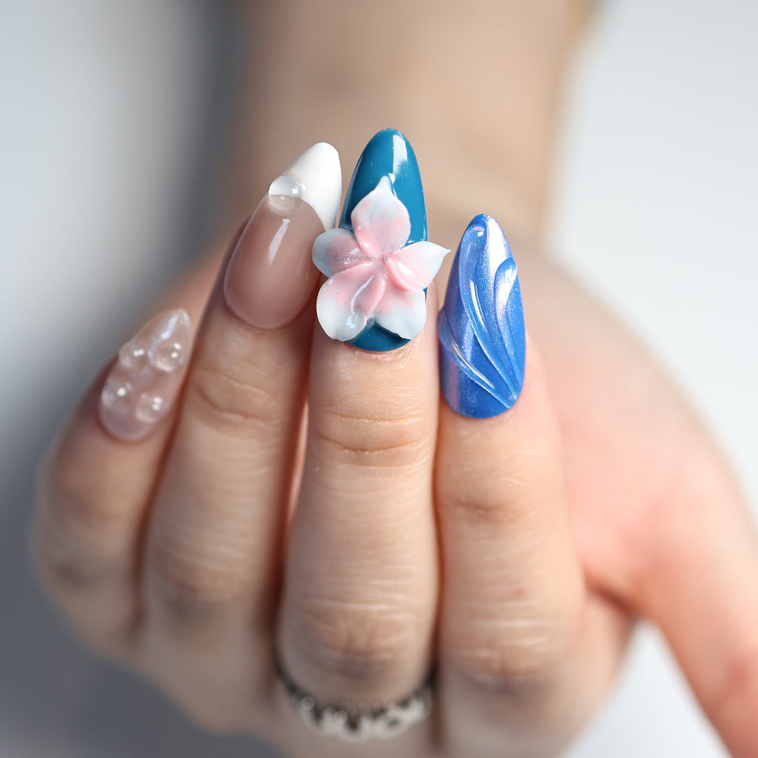 Petal Waves press-on nails worn on hand, with blue and pastel tones, pink 3D flower, glossy raised details, and bubble accents