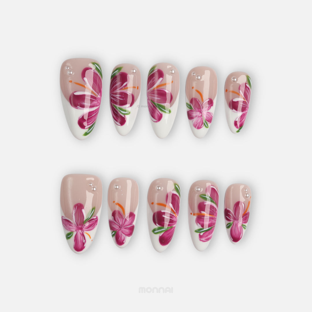 Pink Breeze press-on nails laid out, soft nude and white floral set with pink flowers, green leaves, and rhinestone accents