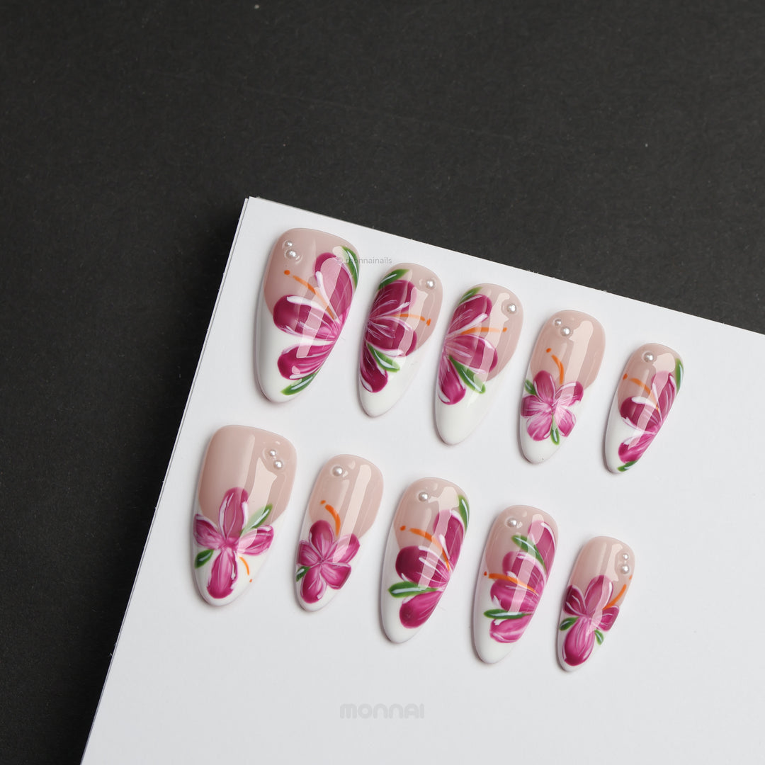 Pink Breeze press-on nails laid out in close-up, with nude and white floral design, pink flowers, green leaves, and rhinestone accents