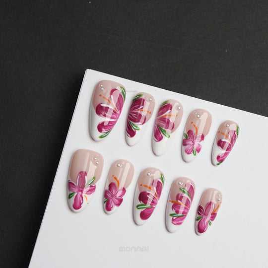 Pink Breeze press-on nails laid out in close-up, with nude and white floral design, pink flowers, green leaves, and rhinestone accents