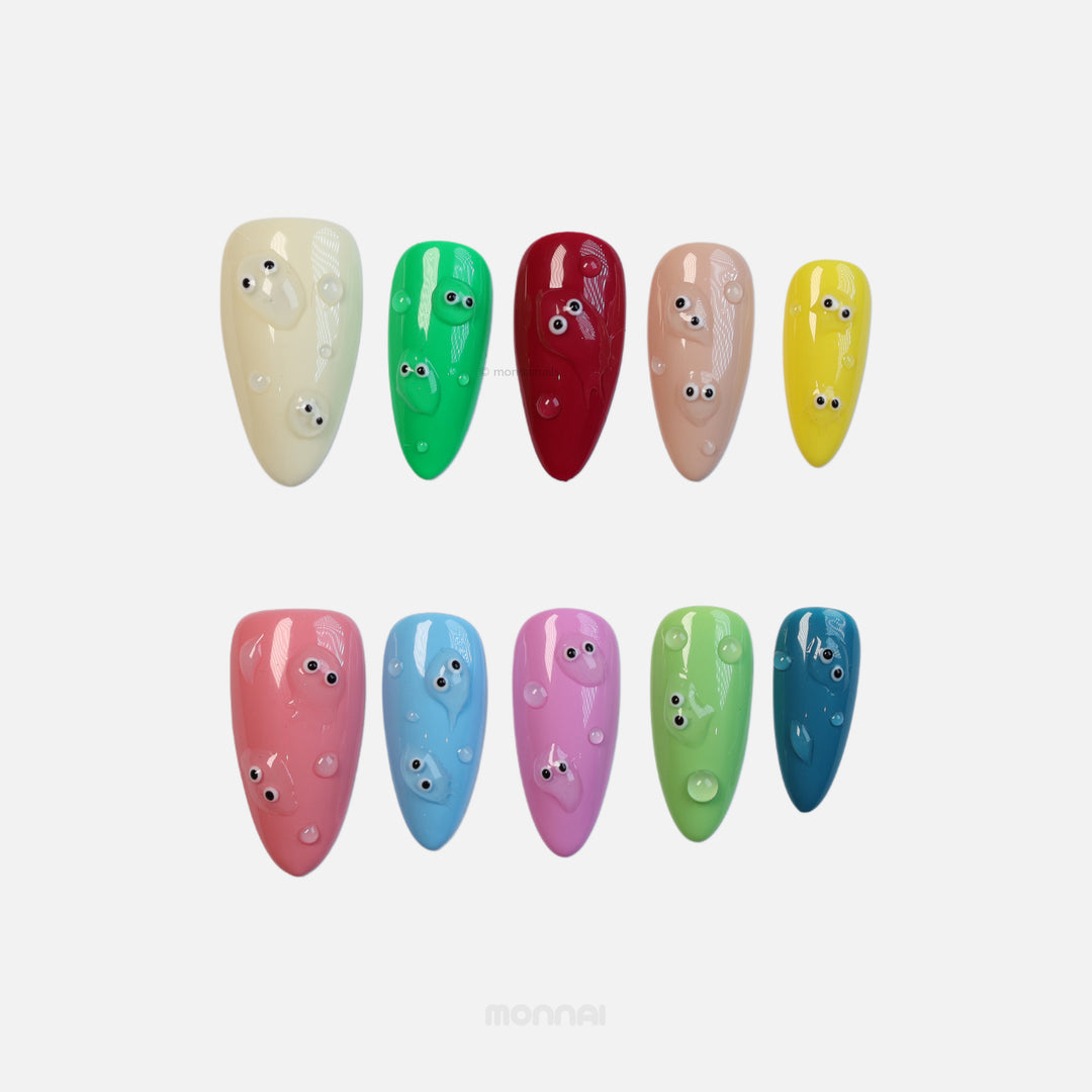 Playful press-on nails laid out in glossy solid colors with tiny bubble-like droplets and eyes, quirky and colorful.