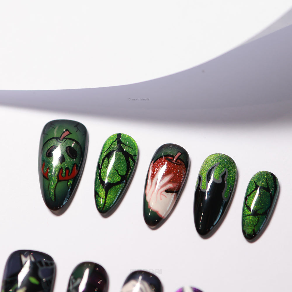Poison Apple press-on nails laid out, featuring dark magic art on vibrant green cat eye bases with a glossy finish.