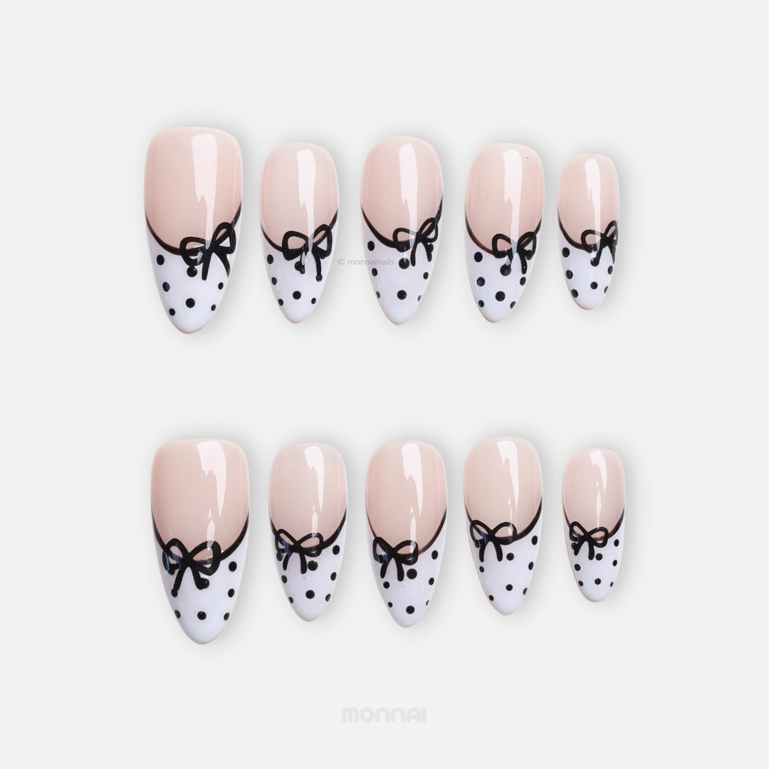 Polka Charm press-on nails laid out with sheer nude bases, black bows, white French tips, and black polka dots.