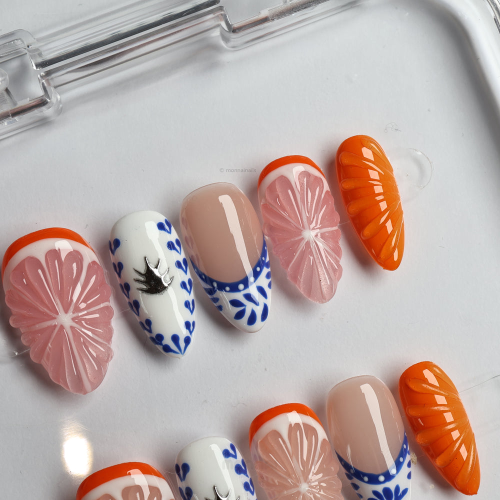 Porcelain Orchard press-on nails laid out with pink grapefruit, blue ceramic accents, nude bases, and glossy orange details.