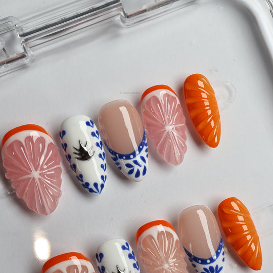 Porcelain Orchard press-on nails laid out with pink grapefruit, blue ceramic accents, nude bases, and glossy orange details.