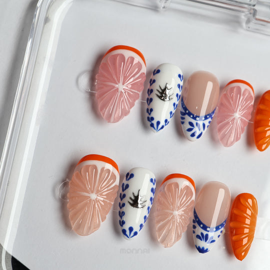 Porcelain Orchard press-on nails laid out with pink grapefruit, blue ceramic accents, nude bases, and bright orange details