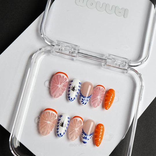 Porcelain Orchard press-on nails laid out in a clear case, with pink citrus, blue ceramic details, and orange accents.
