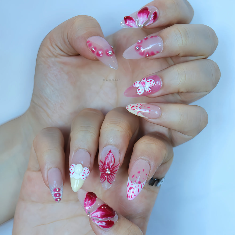 Pretty Petal Party press-on nails on hands with pink floral accents, rhinestones, and pearl flower details