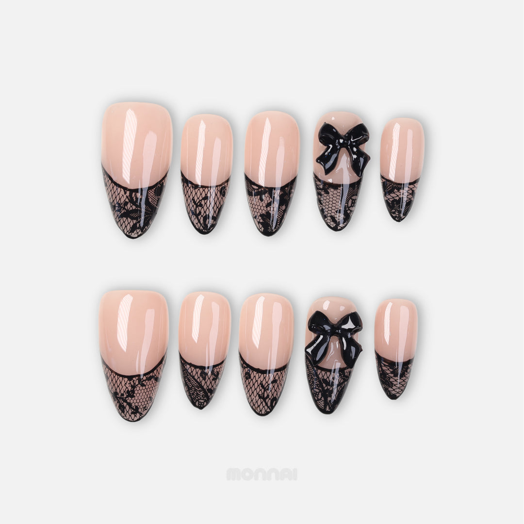 Pretty in Lace press-on nails shown in close-up, nude with black lace French tips and a glossy bow accent.