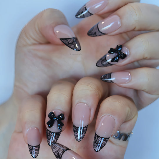 Pretty in Lace press-on nails worn on hands, with sheer nude bases, black lace French tips, and bow accents.