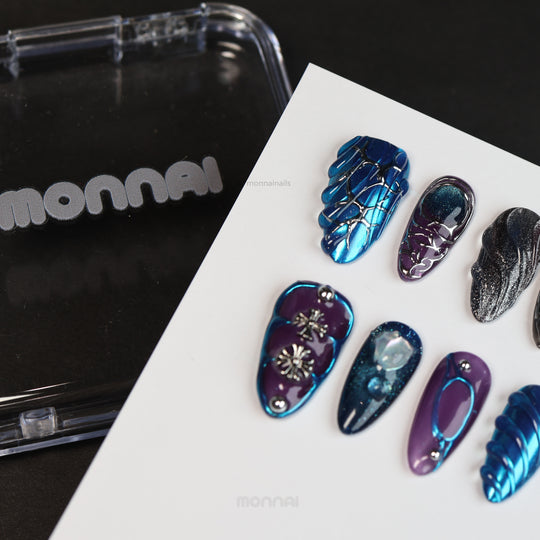 Prometheus press-on nails laid out with metallic blue chrome, purple accents, sculpted textures, and silver cross details